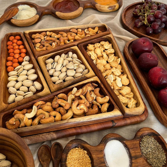 Wooden tray with compartments filled with various nuts and seeds, surrounded by additional fruits and spices.